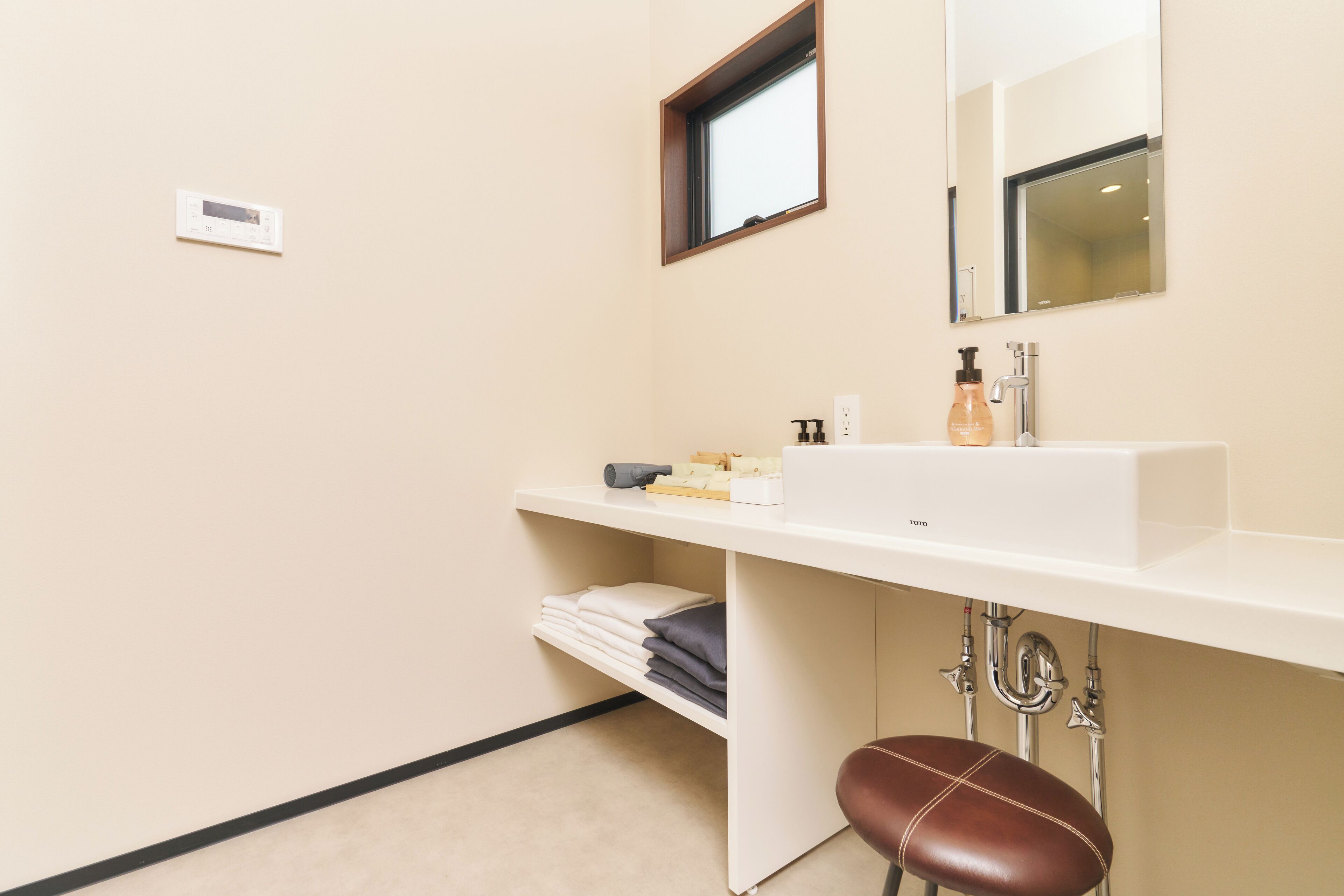 A bathroom with a white sink, mirror, and towel rack. There is a window above the sink and a thermostat on the wall.
