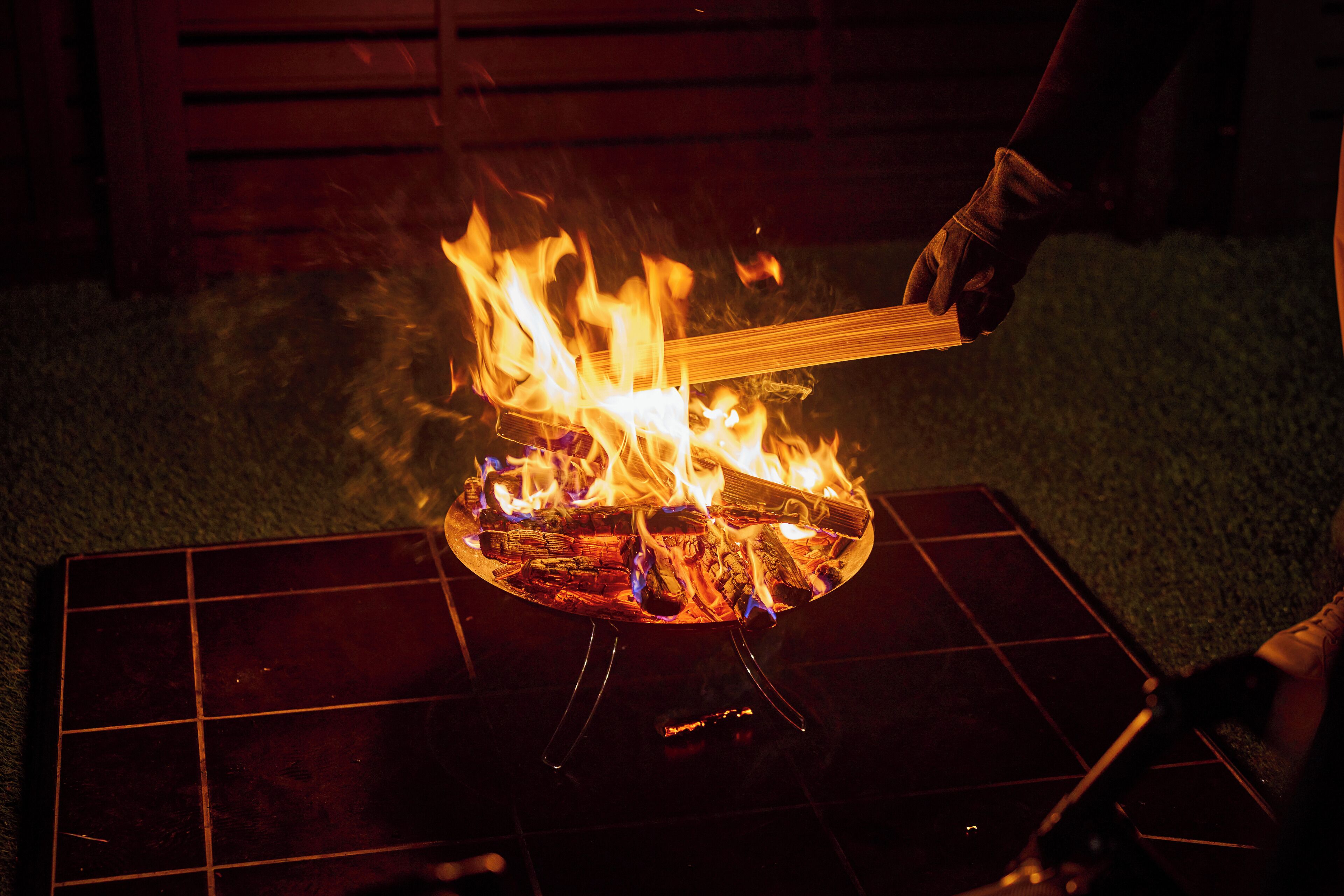 Una persona cuidando un fuego en una parrilla metálica al aire libre de noche.