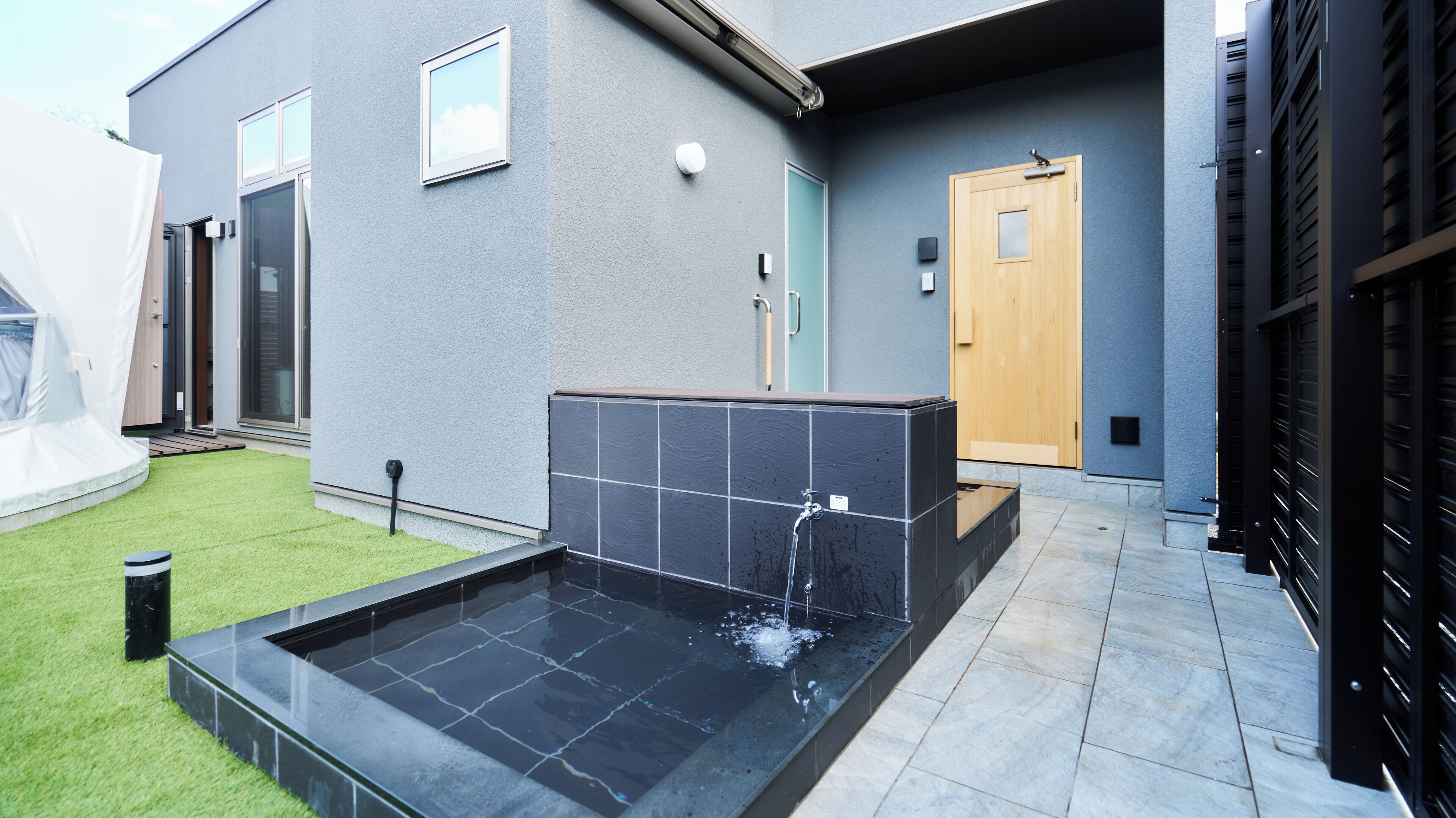 A modern outdoor pool area with a rectangular pool, a wooden door, and a grey building facade.