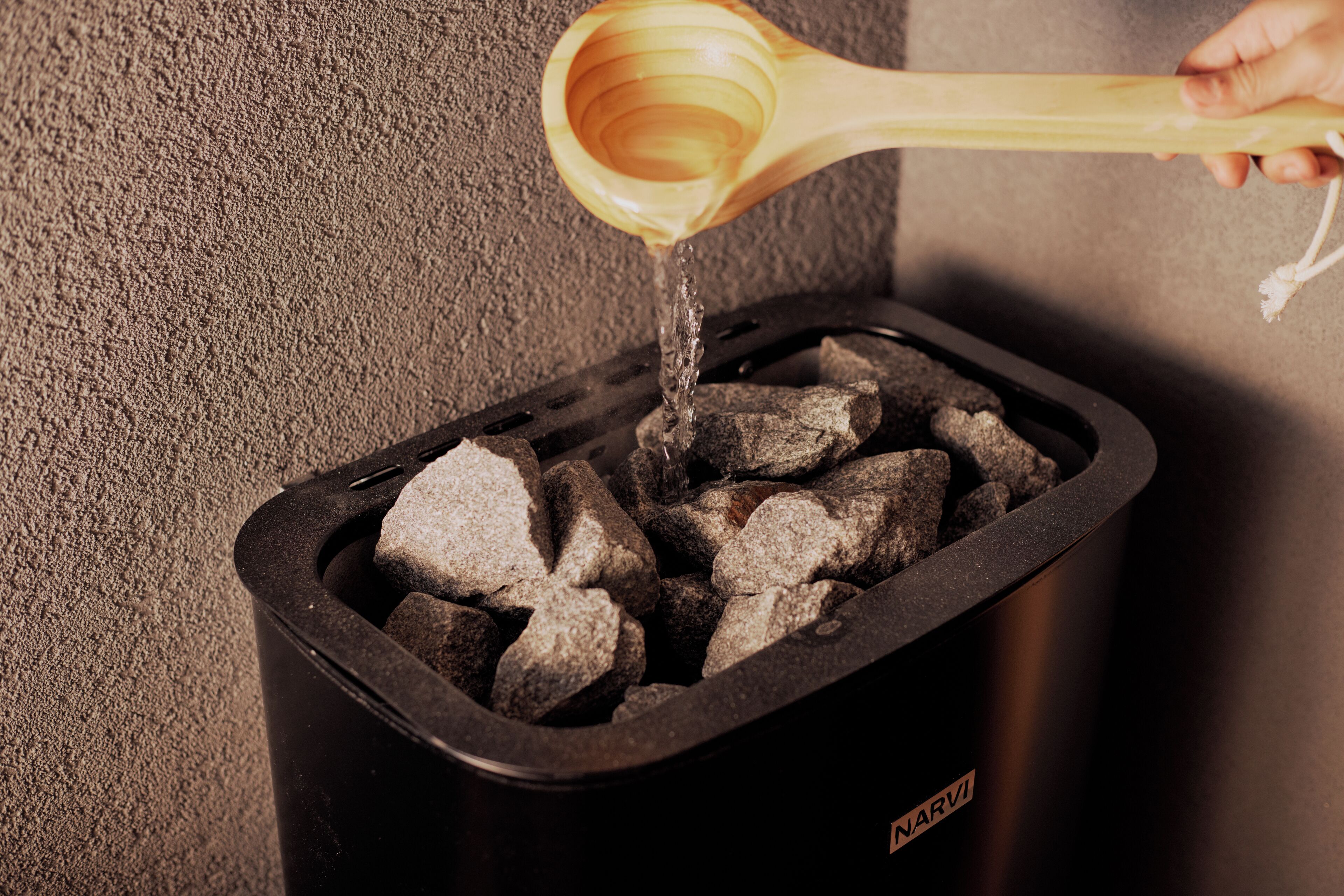 Eine Hand gießt Wasser in einen Behälter für Holzkohle.
