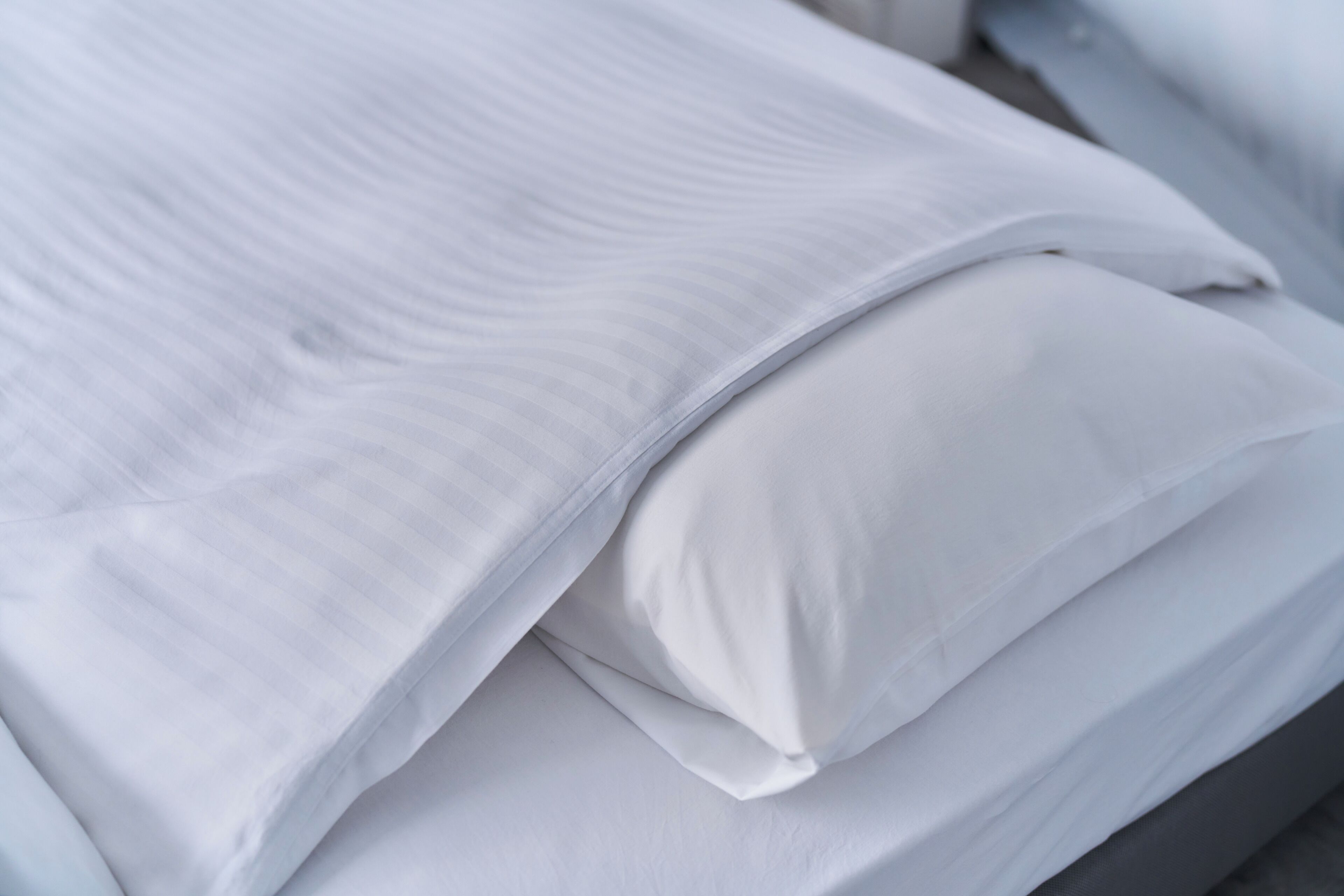 A neatly made bed with white linens and pillows.