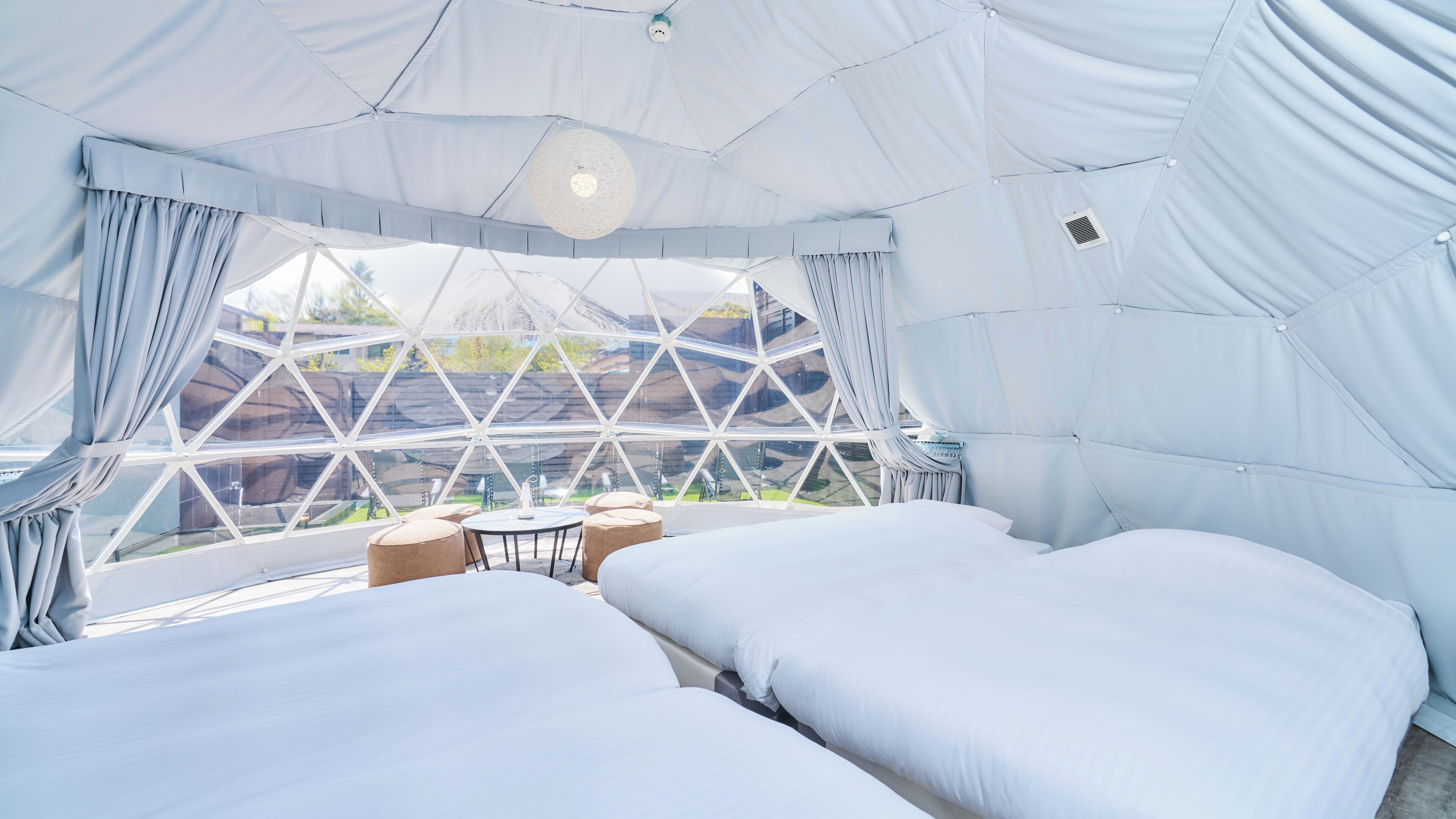 A spacious tented accommodation with two beds, a small table, and a view of the surrounding landscape.
