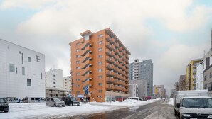 Een meerhoog gebouw met een opvallend hoekig ontwerp, omringd door andere gebouwen en geparkeerde voertuigen.