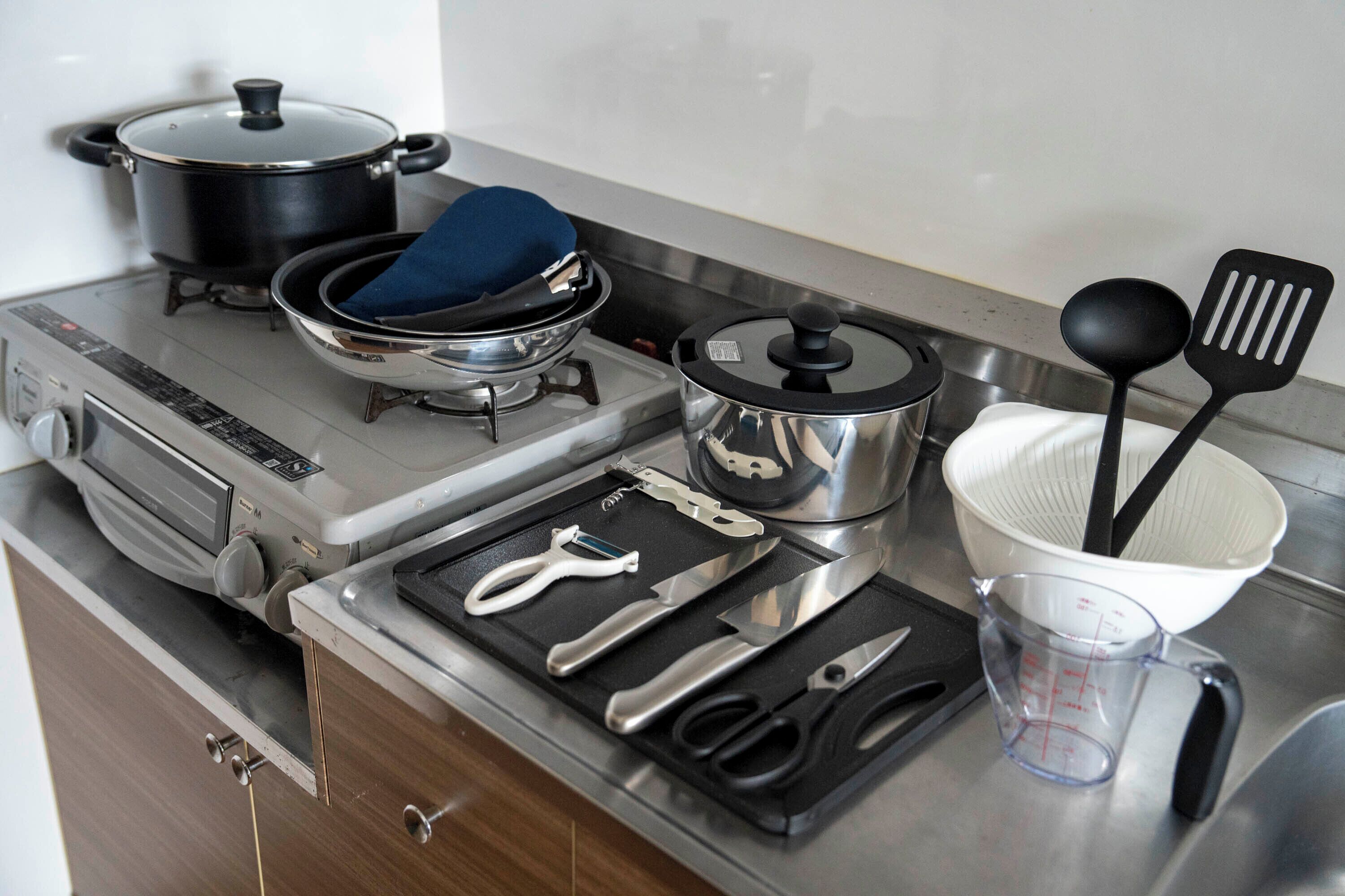 Una cocina con estufa, ollas, un colador y diversos utensilios.