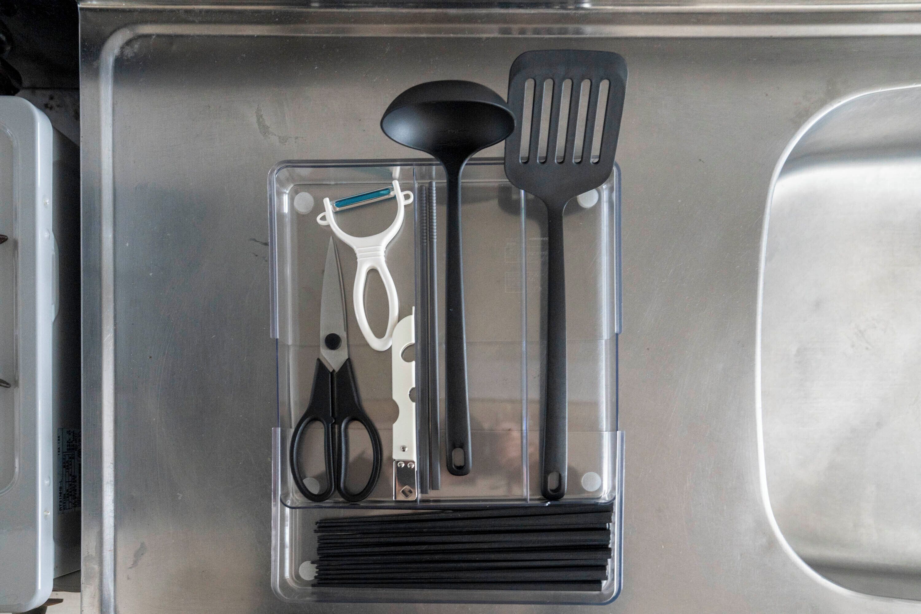 Un lavamanos de cocina con un organizador de utensilios que contiene un par de tijeras, una espátula y un rallador.