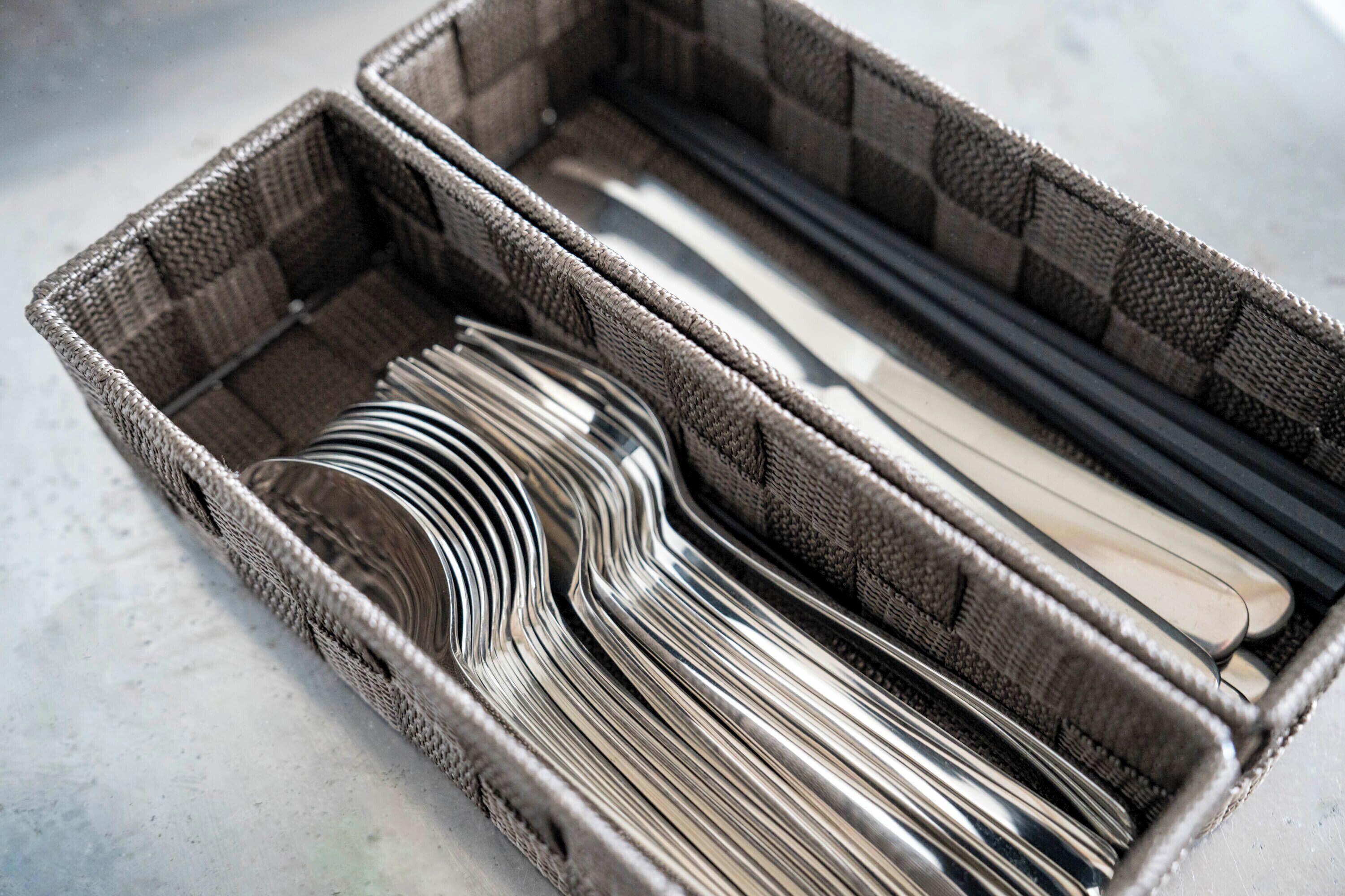 A wicker basket containing neatly folded metal utensils.
