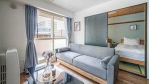 Een moderne hotelkamer met een grijze bank, een houten bedframe, een grote spiegel en uitzicht op de stad door het raam.