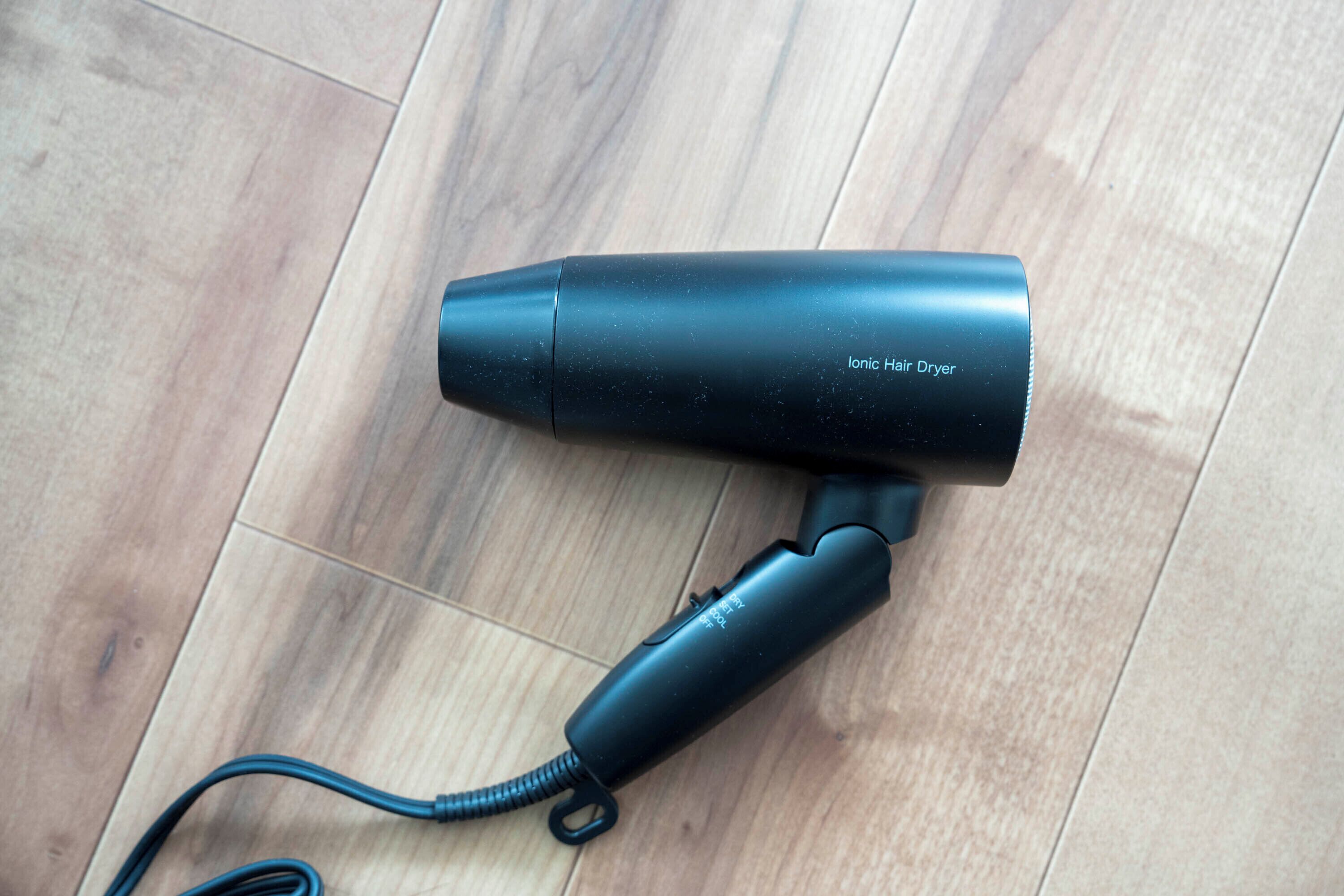 A black ionic hair dryer on a wooden floor.