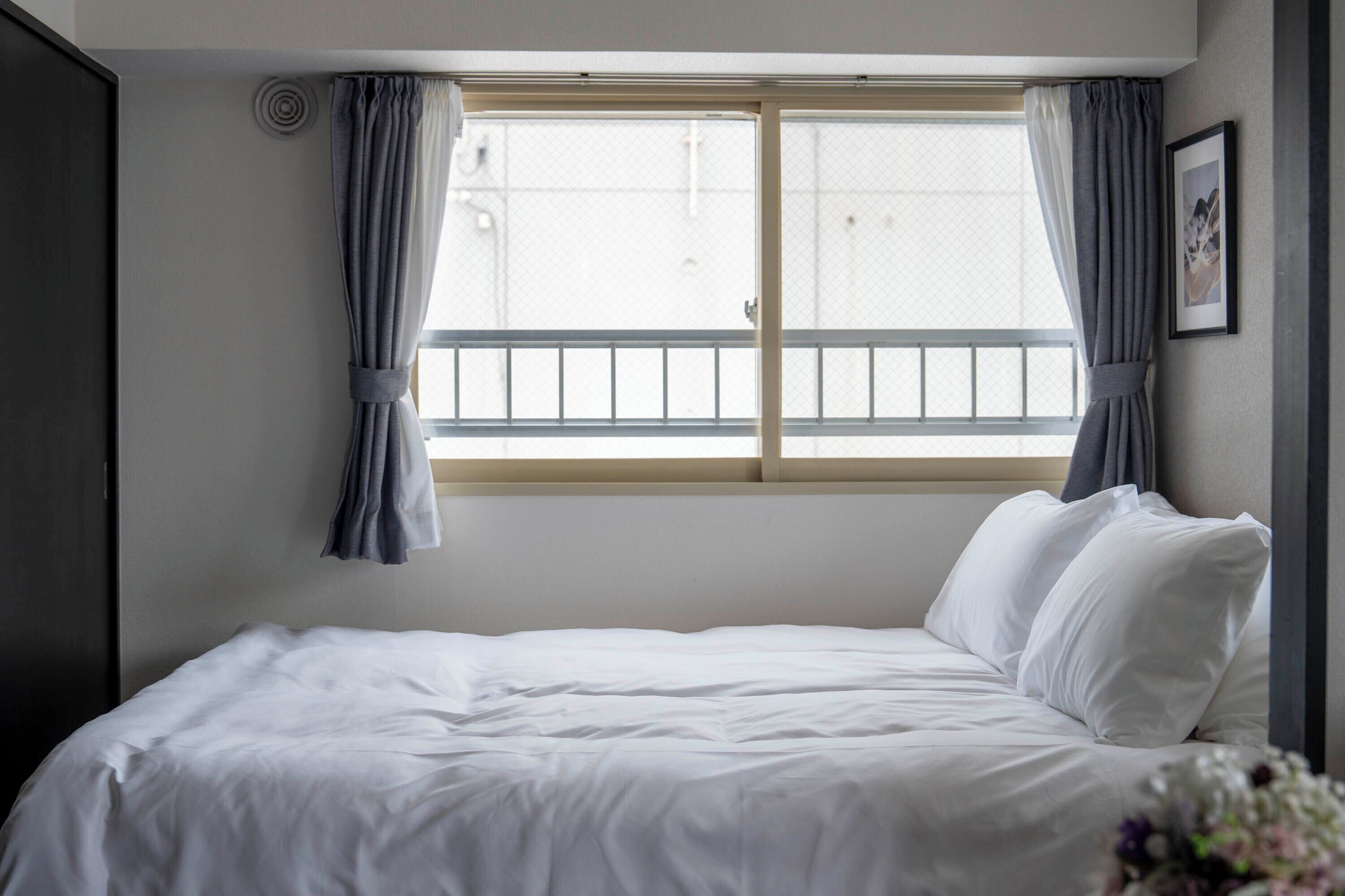A hotel room with a bed, a window with curtains, and a framed picture on the wall.