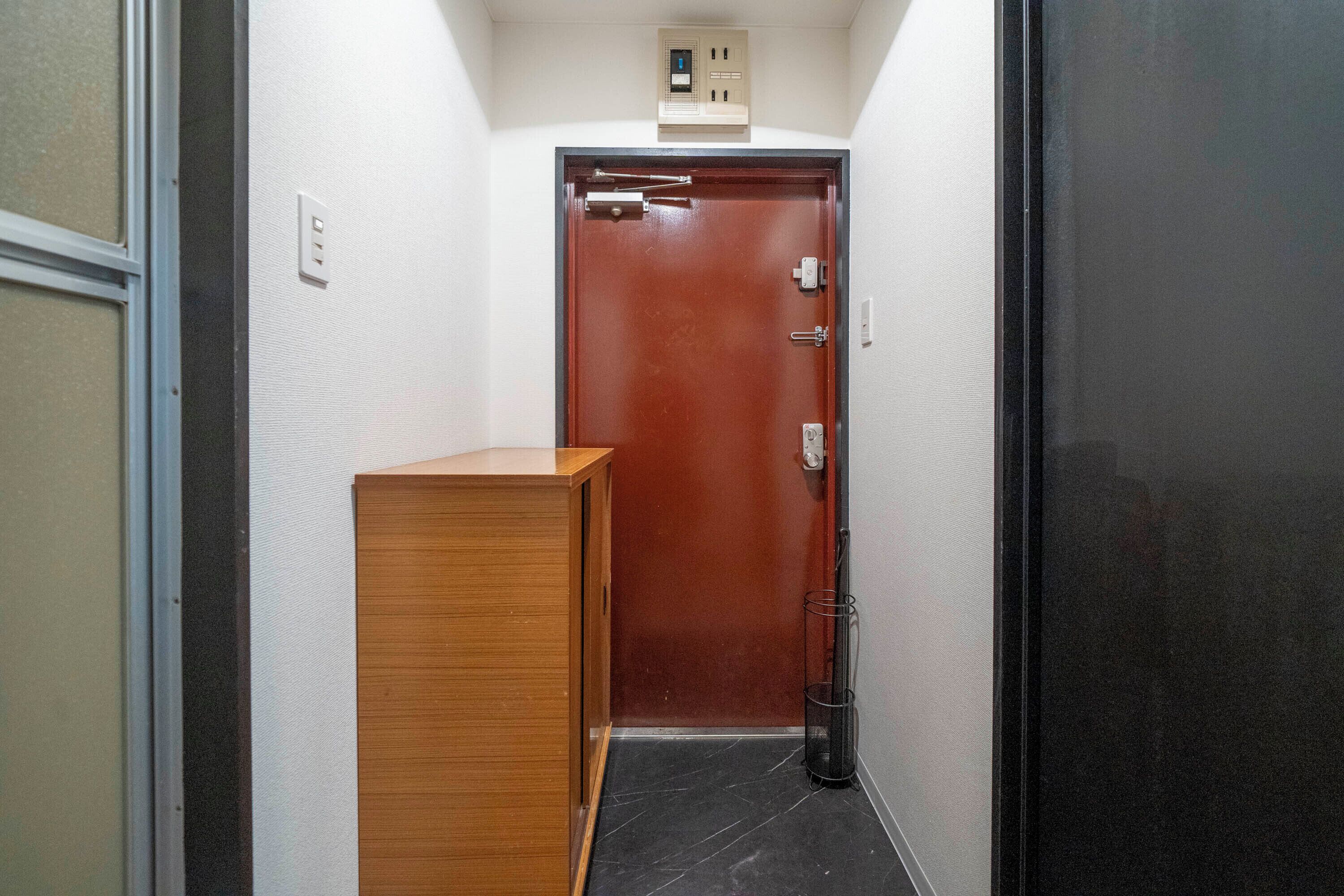 Um corredor estreito com um armário de madeira, uma porta com puxador e uma lixeira.