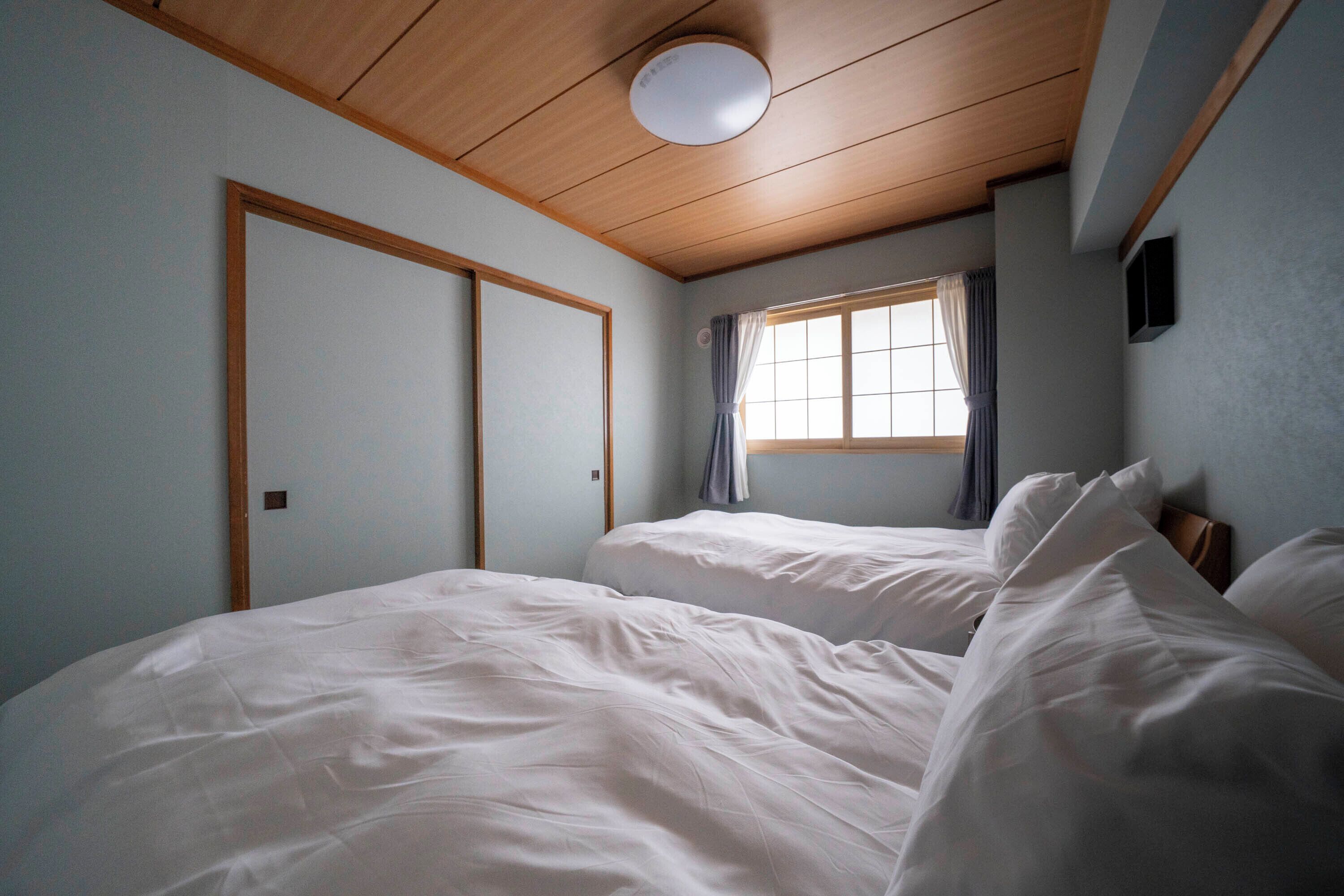 A bedroom with two beds, wooden ceiling, and a window with curtains.
