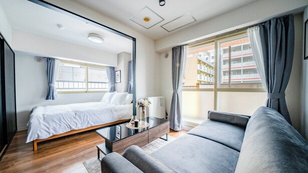 Een moderne hotelkamer met een bed, een slaapbank, een klein tafeltje met een vaas en een raam met gordijnen.