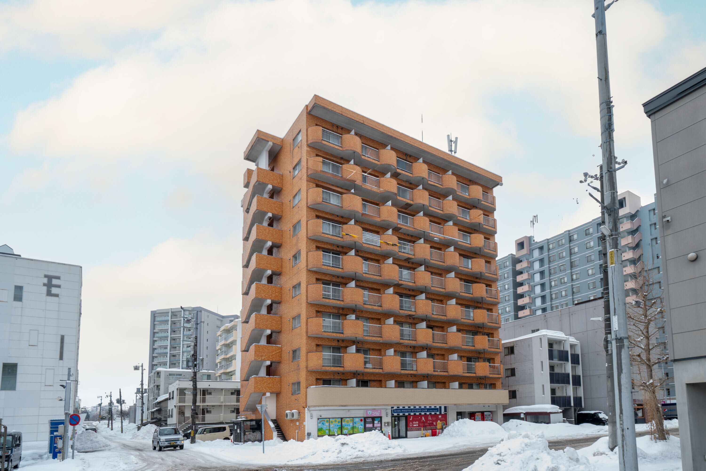 Un immeuble résidentiel à plusieurs étages, doté de balcons, d’une devanture visible et situé dans une rue recouverte de neige.