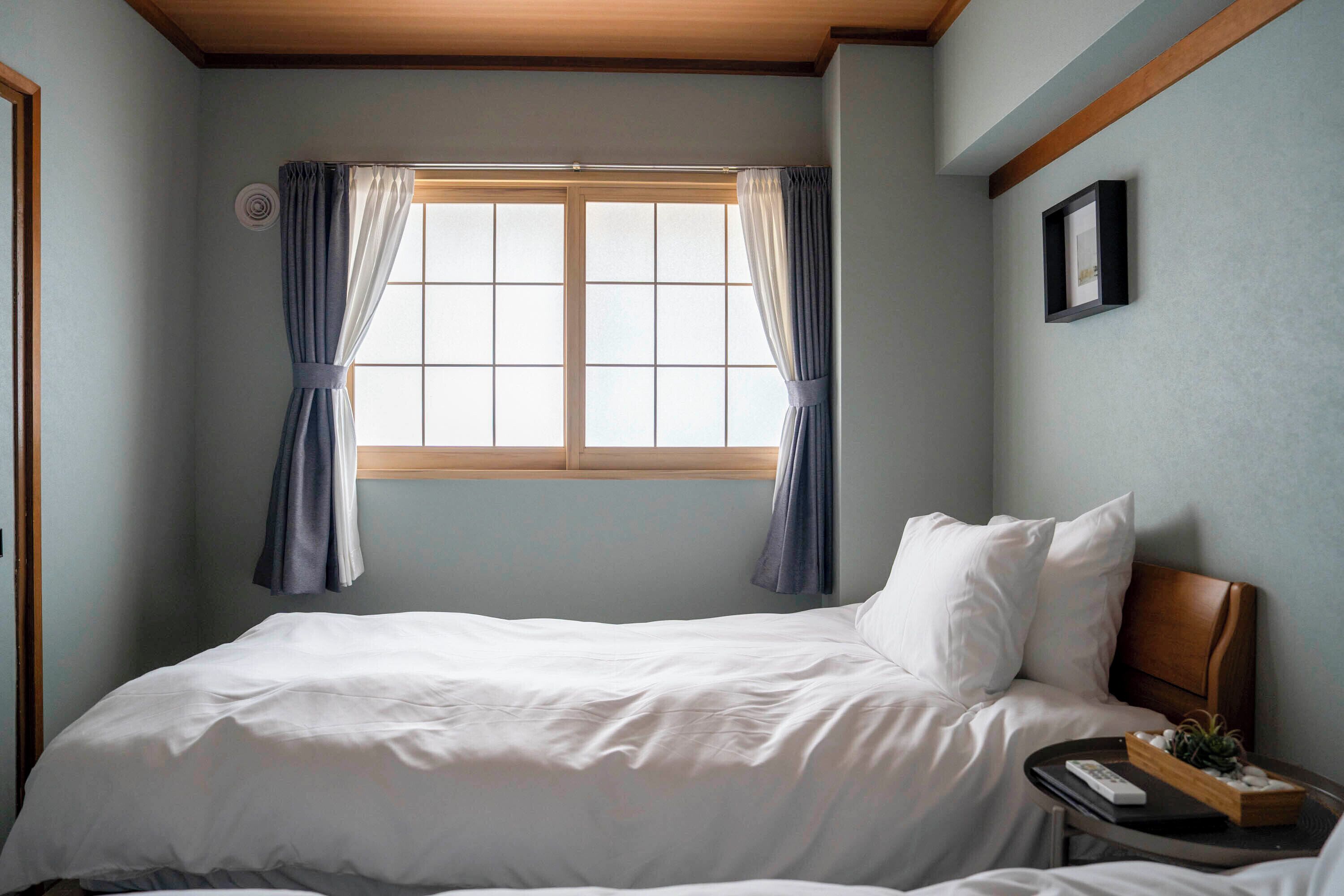 A bedroom with a bed, a nightstand, a window with curtains, and a framed picture on the wall.
