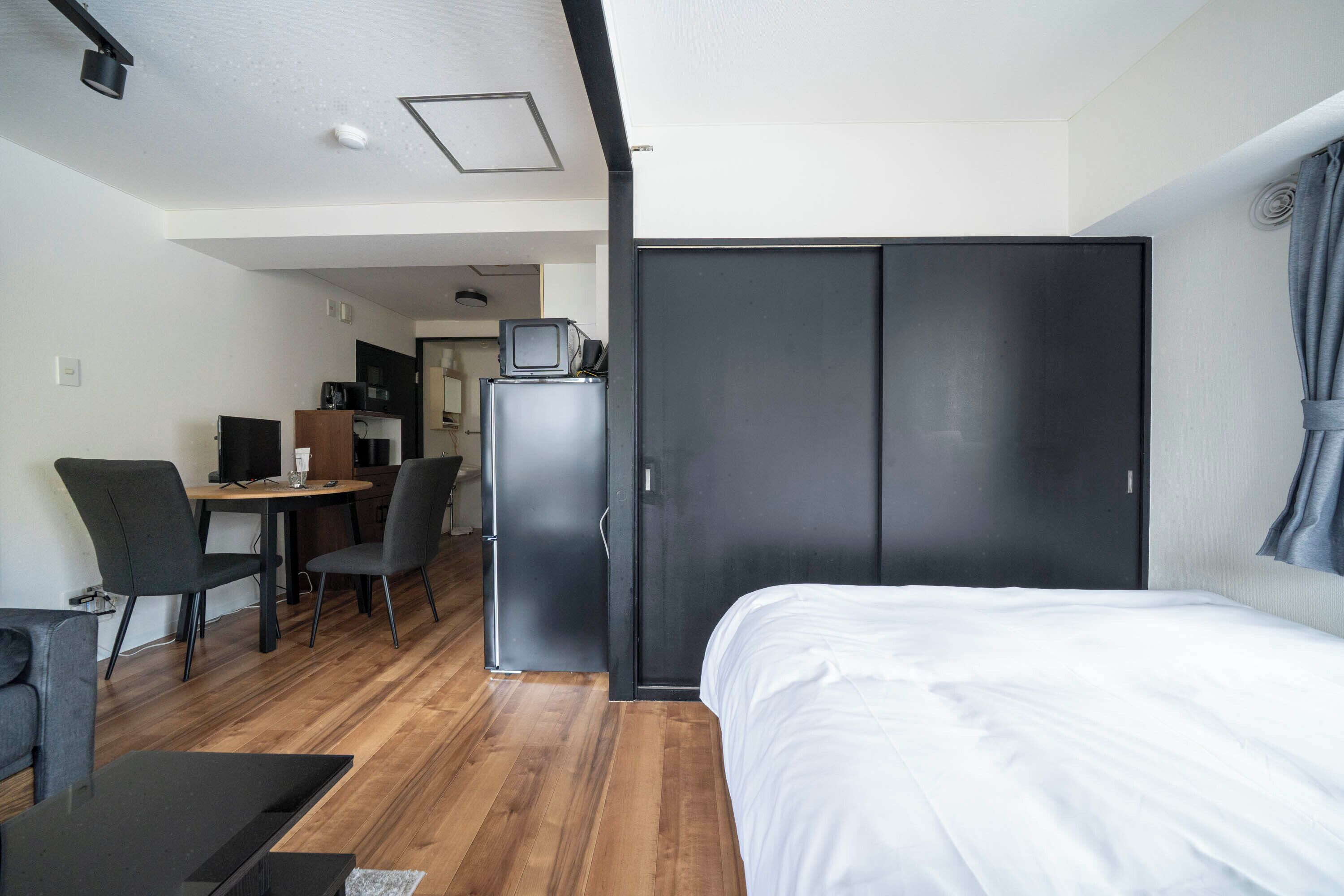 Une chambre d’hôtel moderne équipée d’un lit, d’un bureau avec un ordinateur, d’un réfrigérateur et d’une armoire.