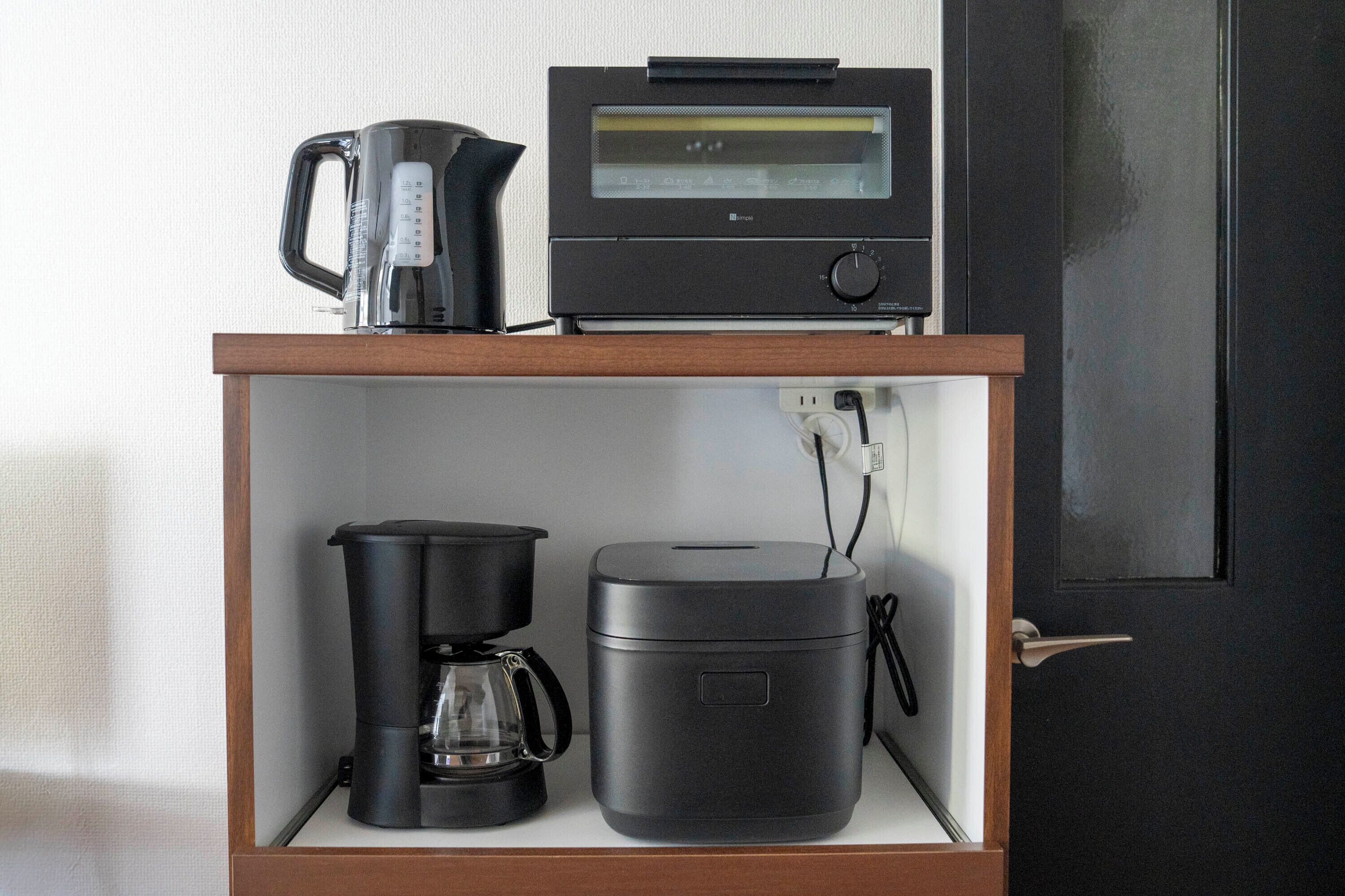 Una kitchenette con cafetera, cocedor de arroz y microondas sobre un estante de madera.