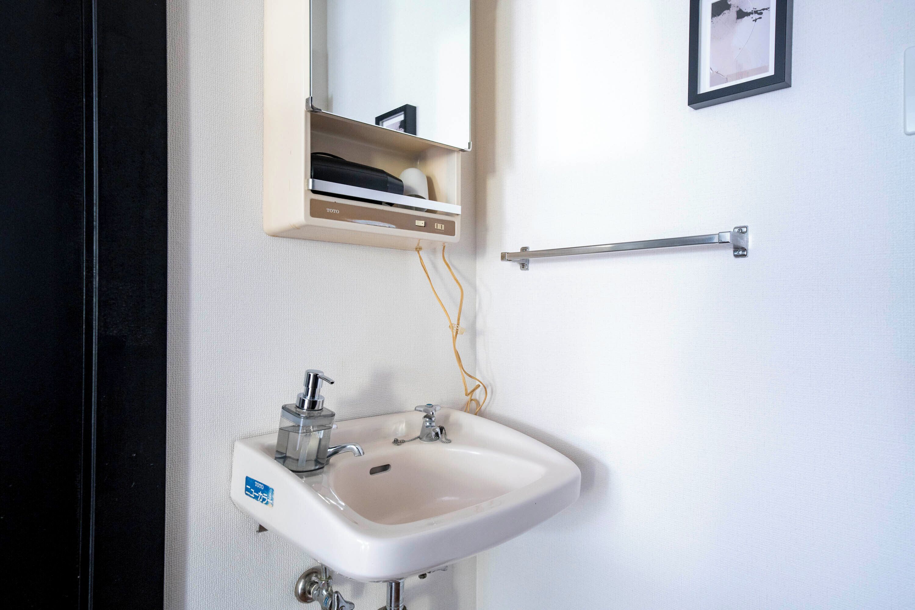Une salle de bain avec un lavabo blanc, un miroir au-dessus et un porte-serviettes sur la droite.