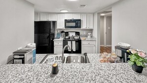 Una cocina compacta con armarios blancos, un refrigerador negro, un microondas y un lavamanos.