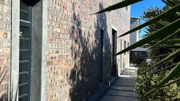 Un stretto vicolo in mattoni con un sentiero in cemento, fiancheggiato da un basso siepe e un edificio con ampie finestre.