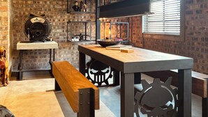 A rustic interior with exposed brick walls, a wooden bench, a table with a skull design, and a hanging light fixture. - The Citadel @ Tether&Tease, Extraordinary BDSM Location in Cape Town (Cape Town)
