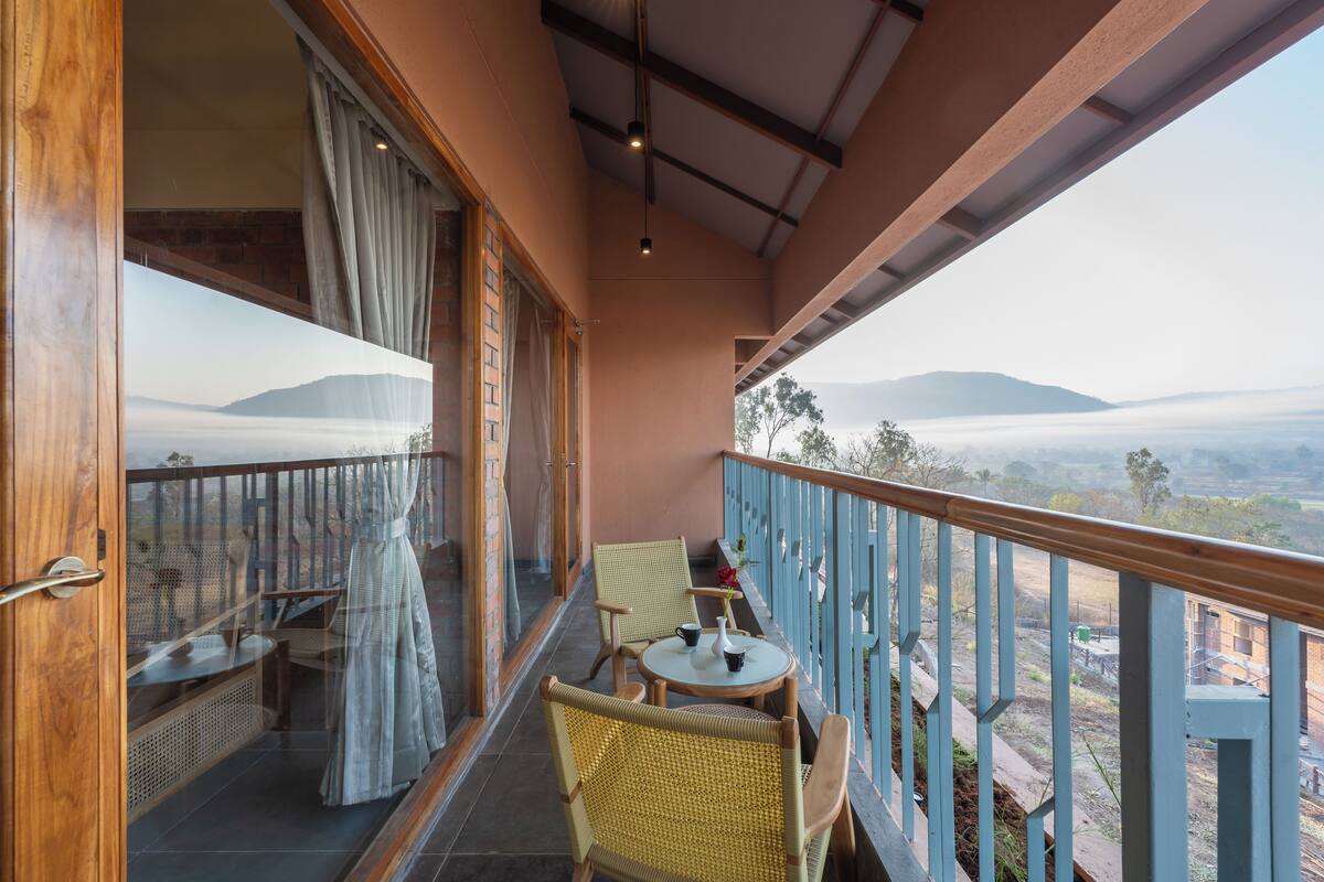 A balcony with wicker chairs, a small round table, and a view of distant mountains.