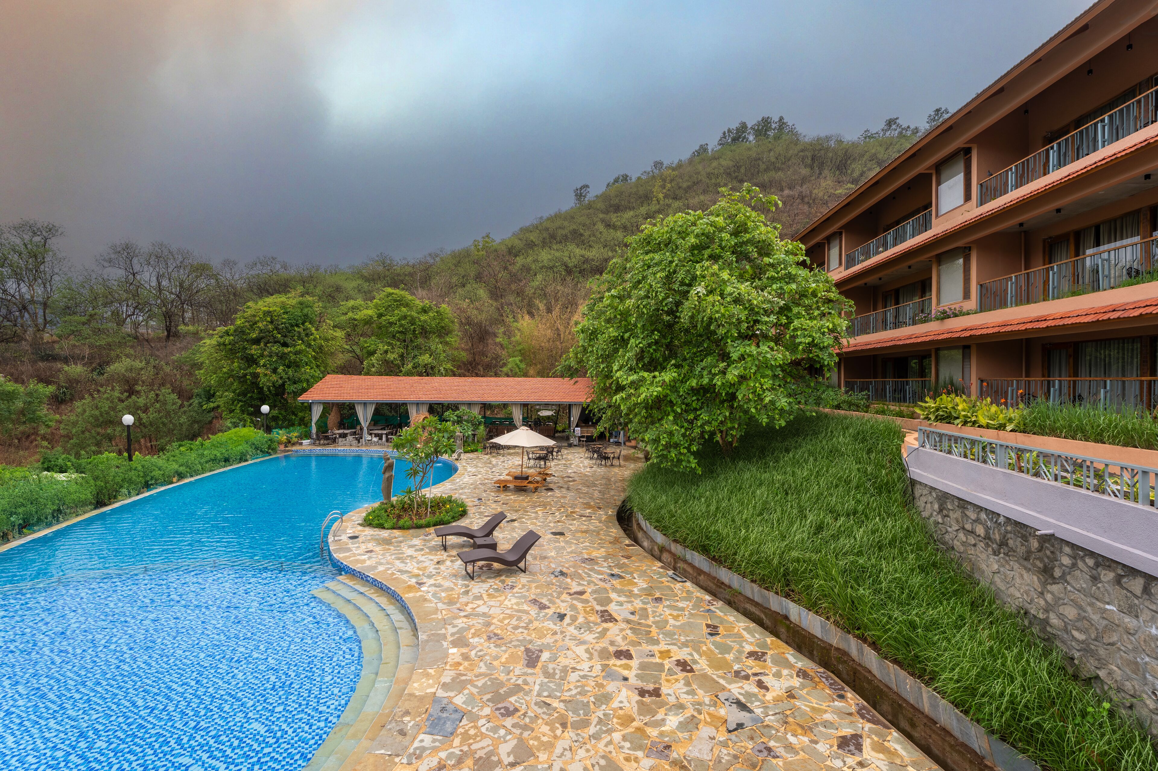 A hotel with a swimming pool, outdoor seating, and a view of a hillside.