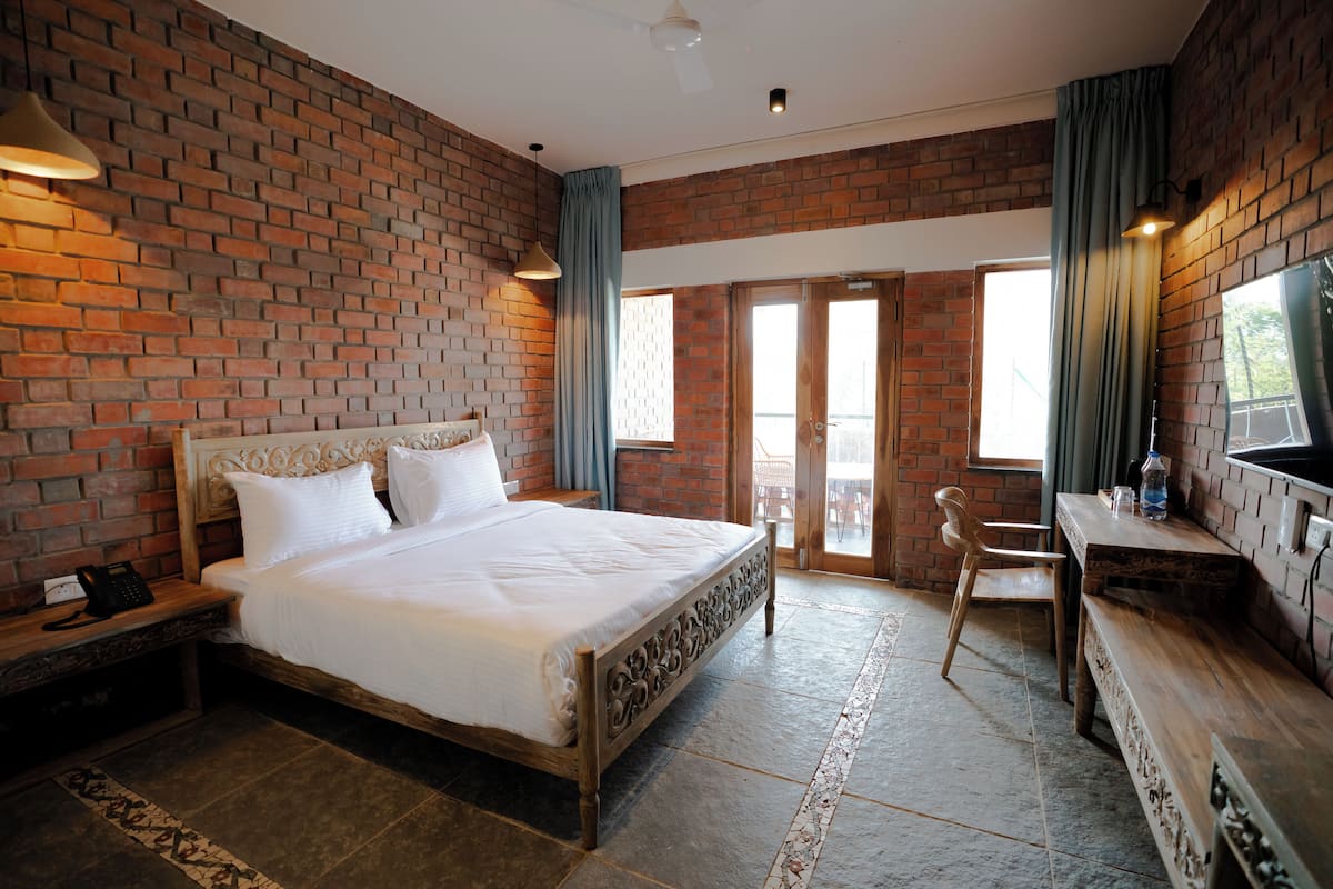 A hotel room with a brick wall, a large bed with white linens, a wooden desk, and a television.