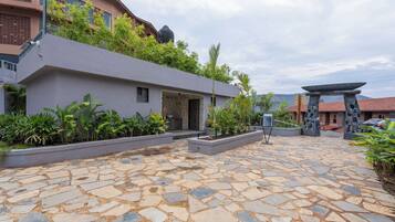 A stone-paved courtyard with a modern building, greenery, and a traditional stone structure.