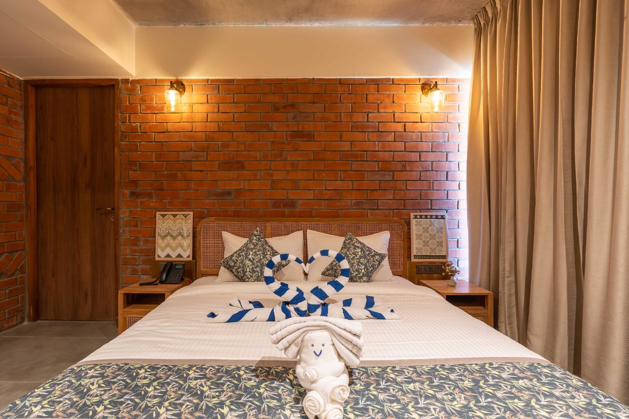 A hotel room with a brick wall, a bed with a striped blanket, pillows, and a decorative towel on the bed.