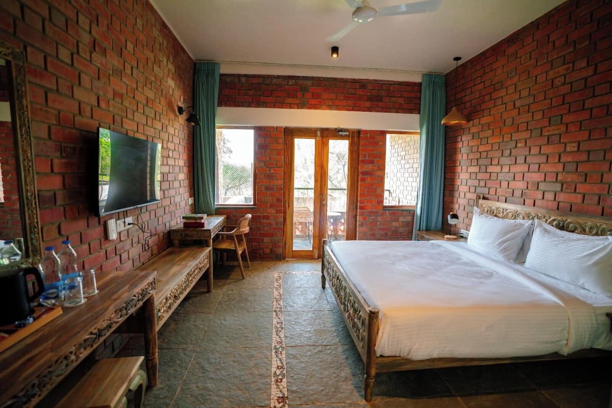 A bedroom with a brick wall, a bed, a desk, a chair, a television, and a window.
