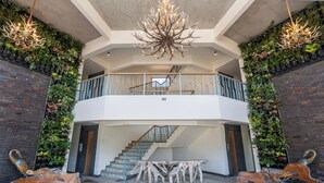 A spacious interior with a central staircase, a chandelier, and a wooden bench.