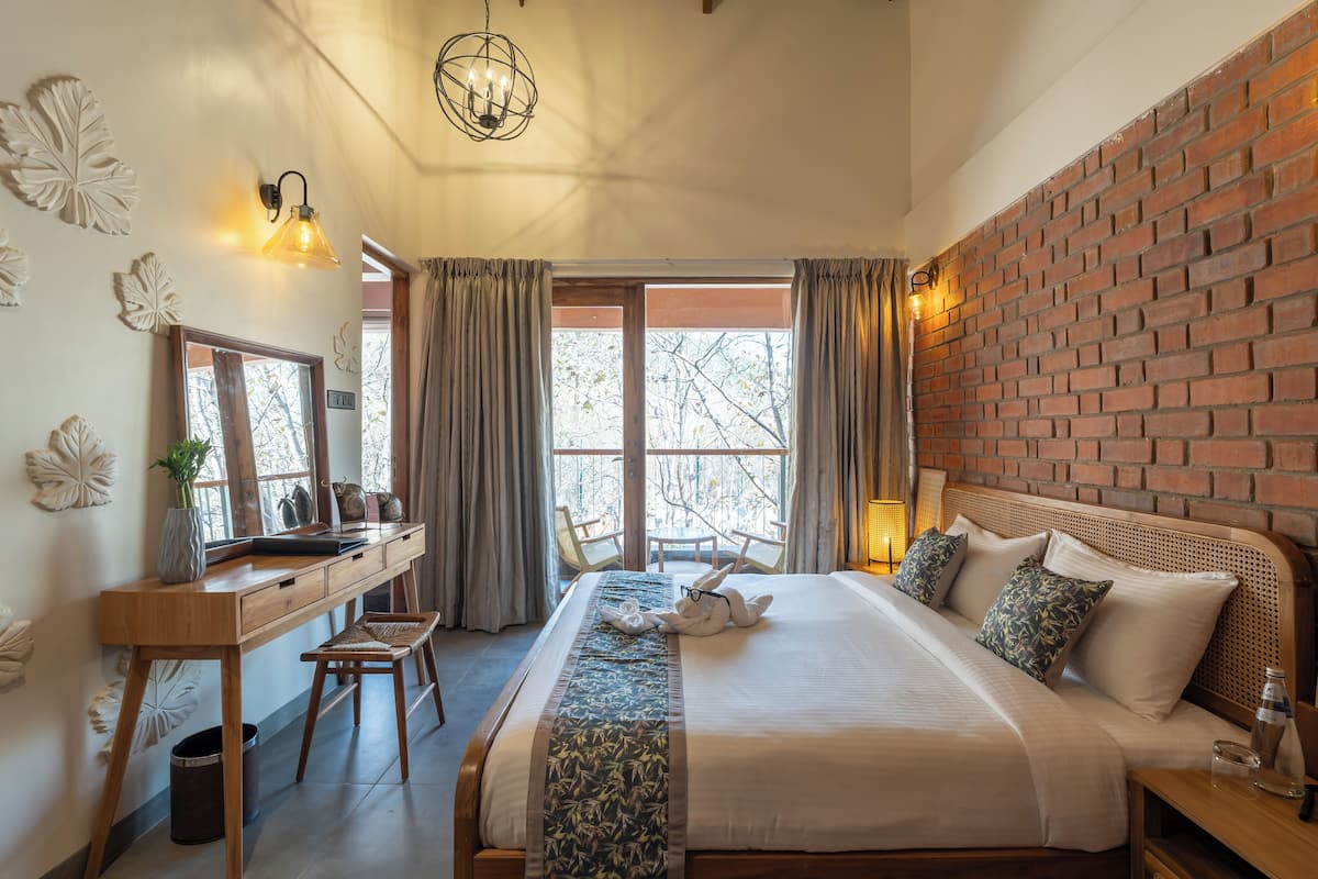 A hotel room with a large bed, a desk, a chair, a mirror, and a brick wall.