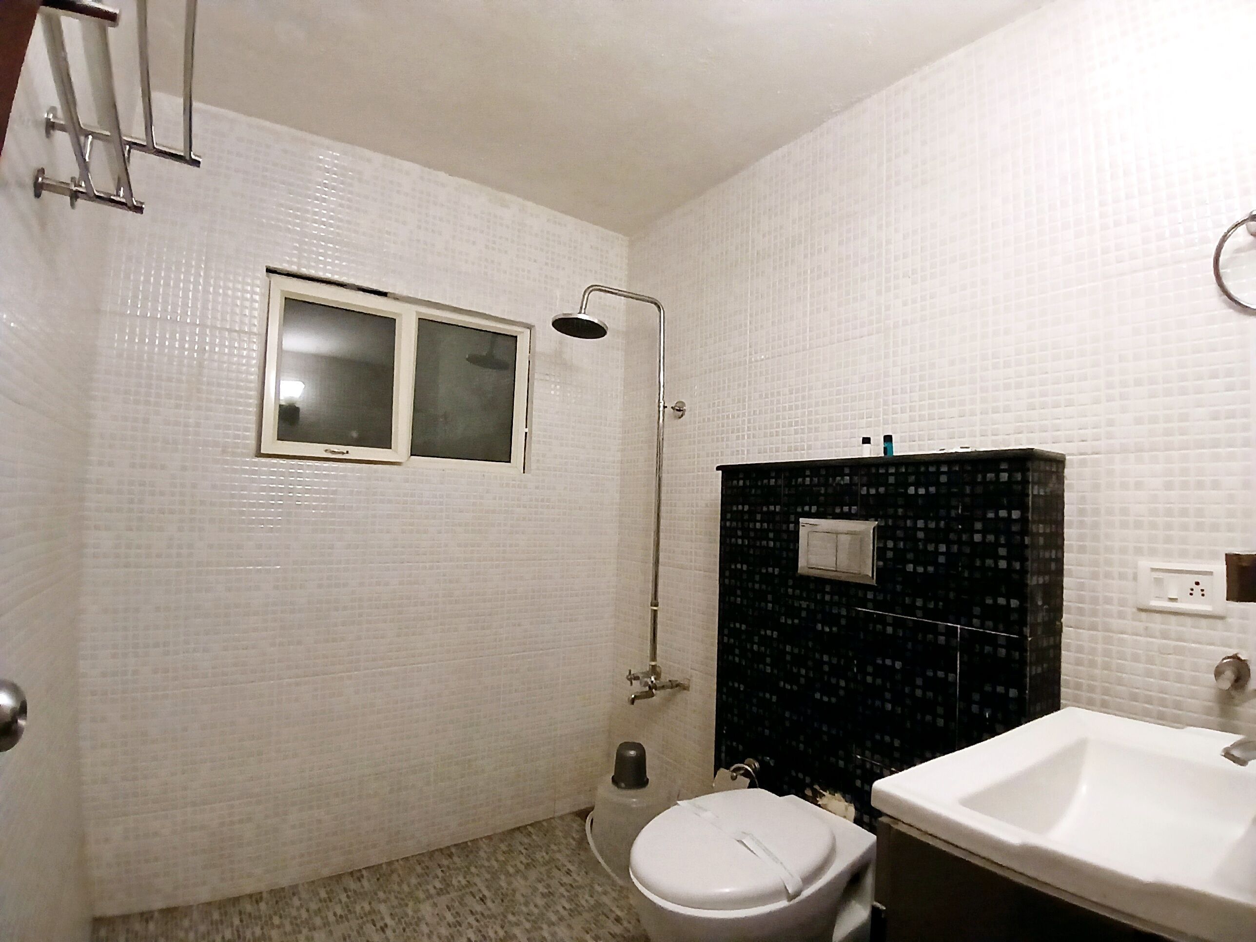 Et badeværelse med hvide flisemure, et bruseområde med sorte fliser, et hvidt toilet og en hvid vask.