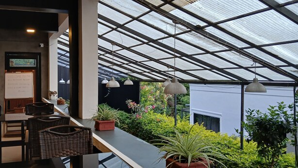 A restaurant with a terrace, wicker furniture, and potted plants. - Veu Munnar Retreat (Devikolam)