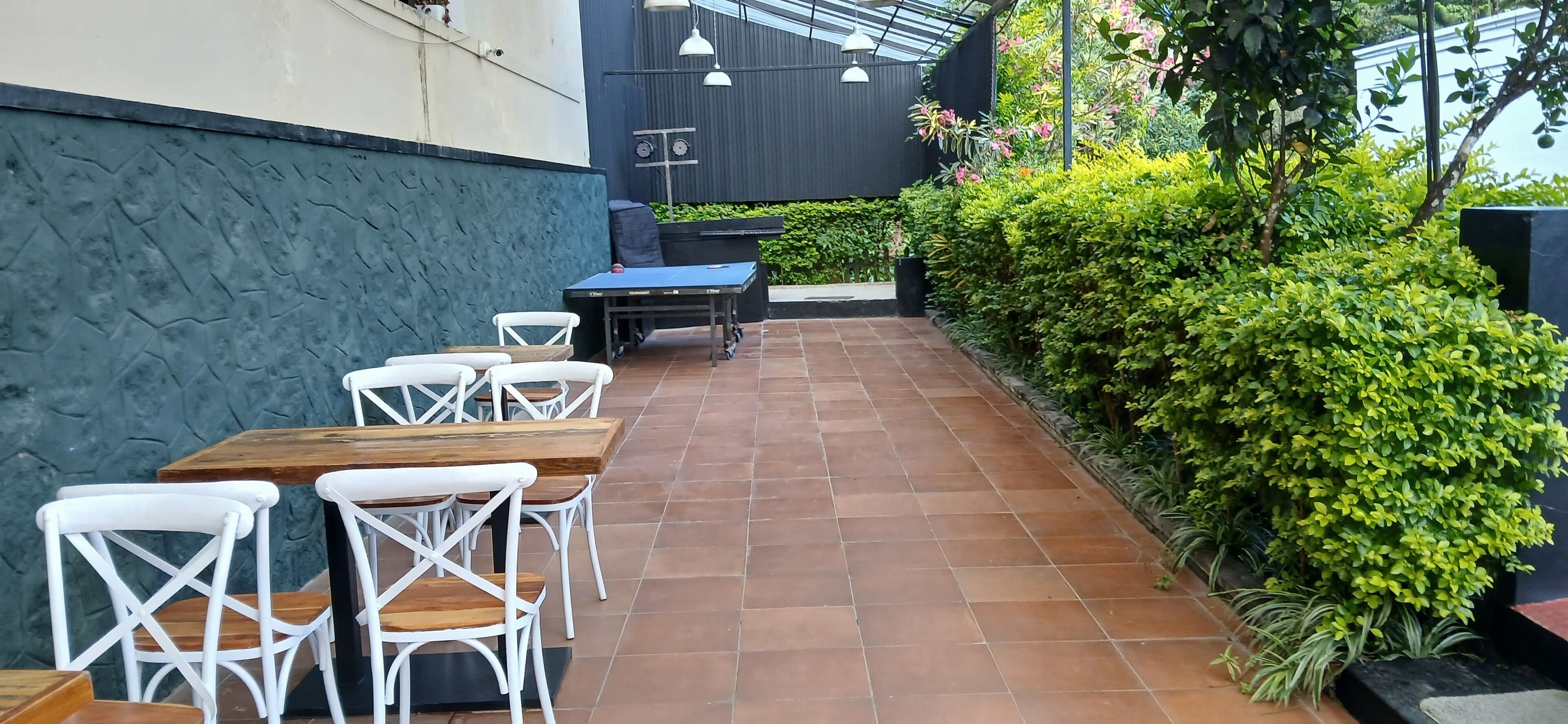 Eine Außenpatio mit Tischen und Stühlen, umgeben von Grünpflanzen und einem modernen Gebäude.