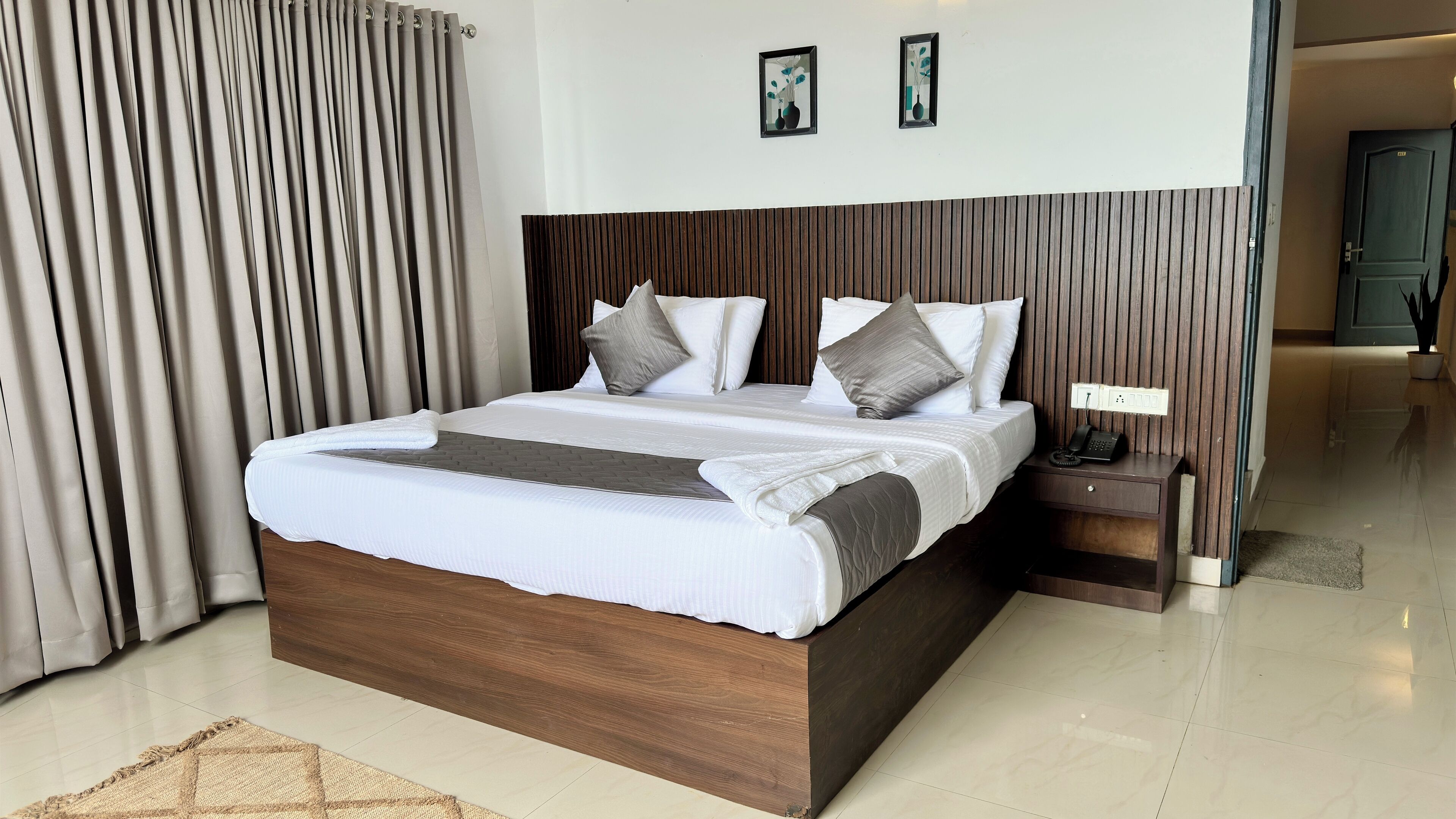 A modern bedroom with a large bed, wooden headboard, and a bedside table with a phone.