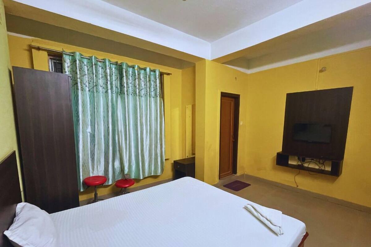 A hotel room with a bed, a TV mounted on the wall, a wardrobe, and a window with curtains.