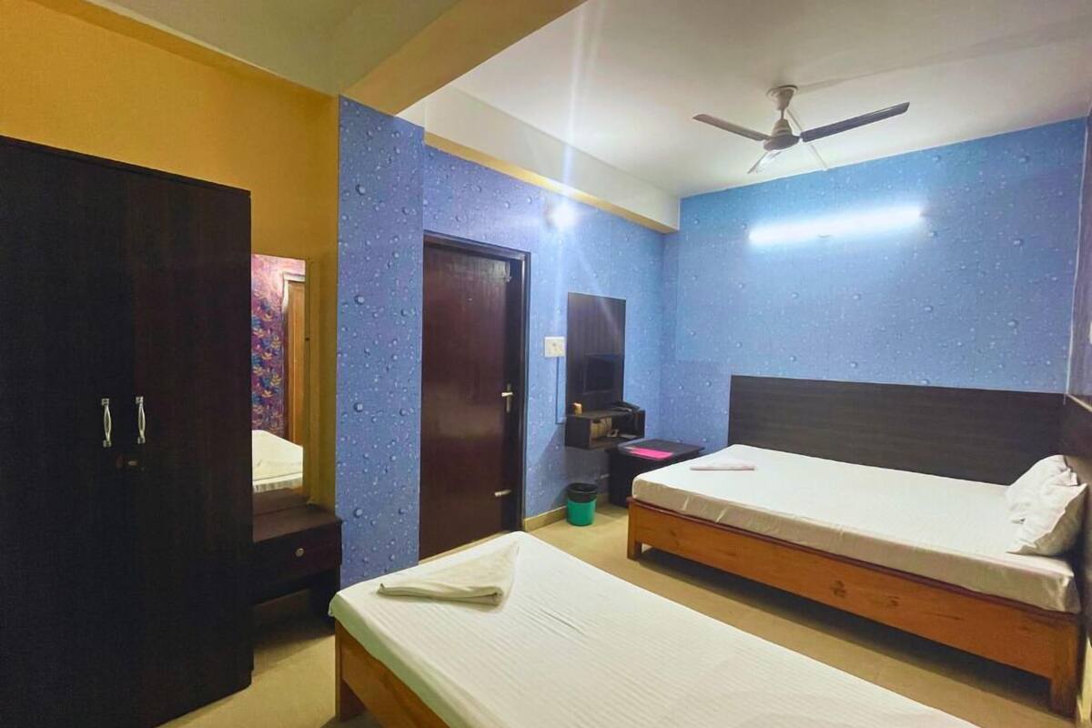 A hotel room with two single beds, a wardrobe, a door, a ceiling fan, and a small table.