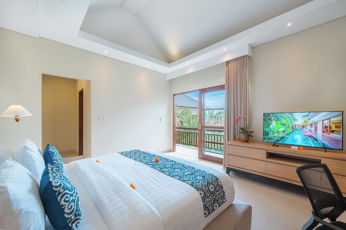 A hotel room with a large bed, a TV, a desk, and a balcony with a view of a swimming pool.