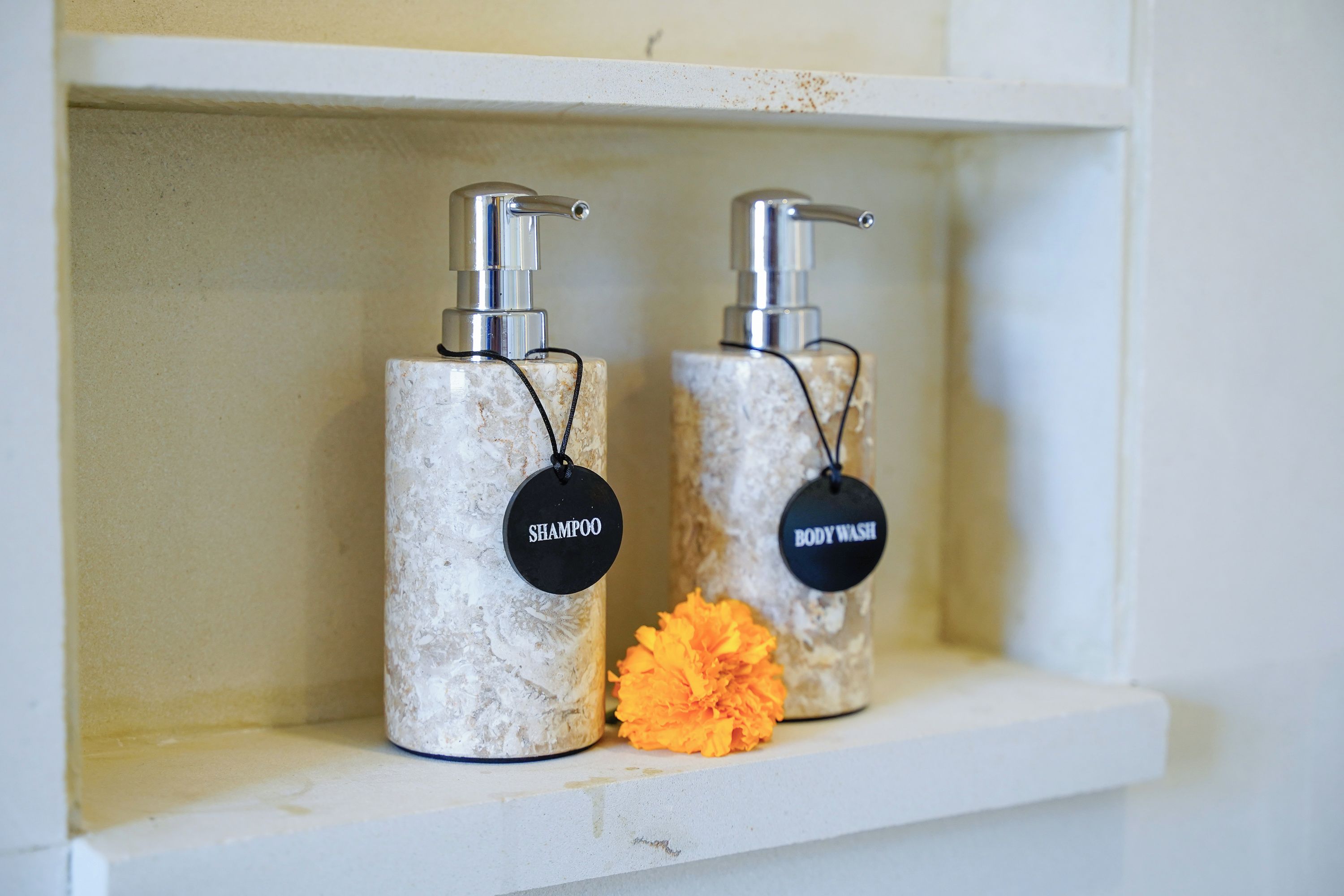 Dos recipientes cilíndricos con dispensadores, etiquetados 'SHAMPOO' y 'BODYWASH', sobre una estantería con superficie blanca.