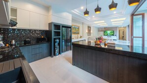 A modern kitchen with dark cabinetry, a black countertop, and a central island. There are overhead pendant lights and a large window providing natural light.