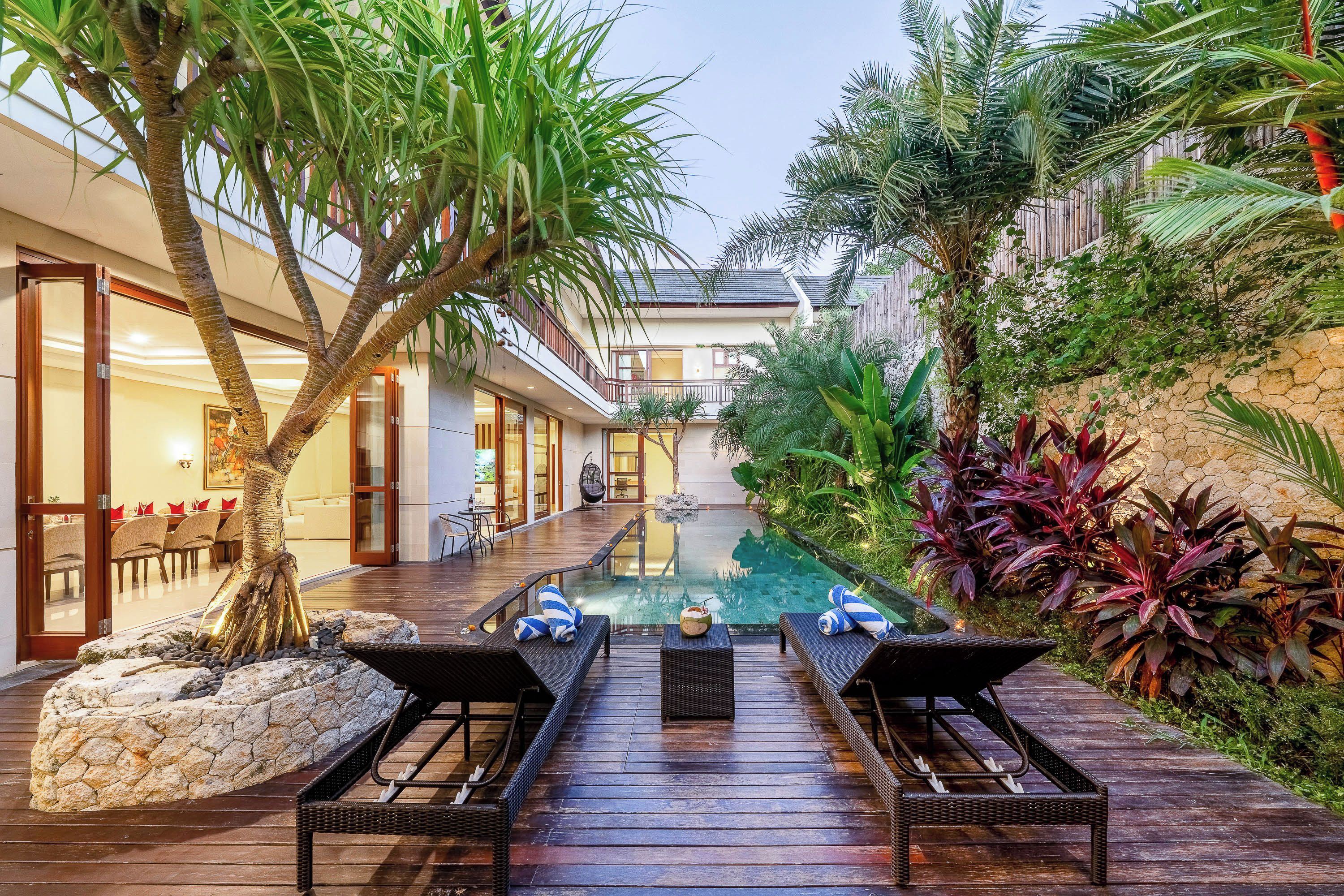 Zona de piscina con sillones de descanso, una pequeña mesa y plantas tropicales.