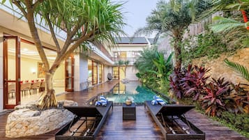 Zona de piscina con sillones de descanso, una pequeña mesa y plantas tropicales.