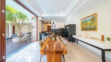 Un comedor amplio con una larga mesa de madera, rodeado de sillas, en una cocina moderna con una isla grande e iluminación colgante.