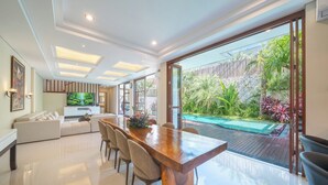 A modern kitchen with a large TV, a dining area with a wooden table and chairs, and a sliding glass door leading to a pool area.