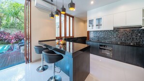 A modern kitchen with a central island, black pendant lighting, and a view of a garden.