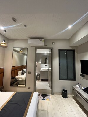 A modern hotel room with a bed, bedside table, mirror, air conditioning unit, and a TV. - Hotel shri anand Vilas (Bhopal)