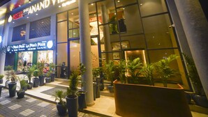 A hotel named "Shri Anand Vilas" with a visible entrance, potted plants, and a sign for "Binoz Pizza" across the street. - Hotel shri anand Vilas (Bhopal)