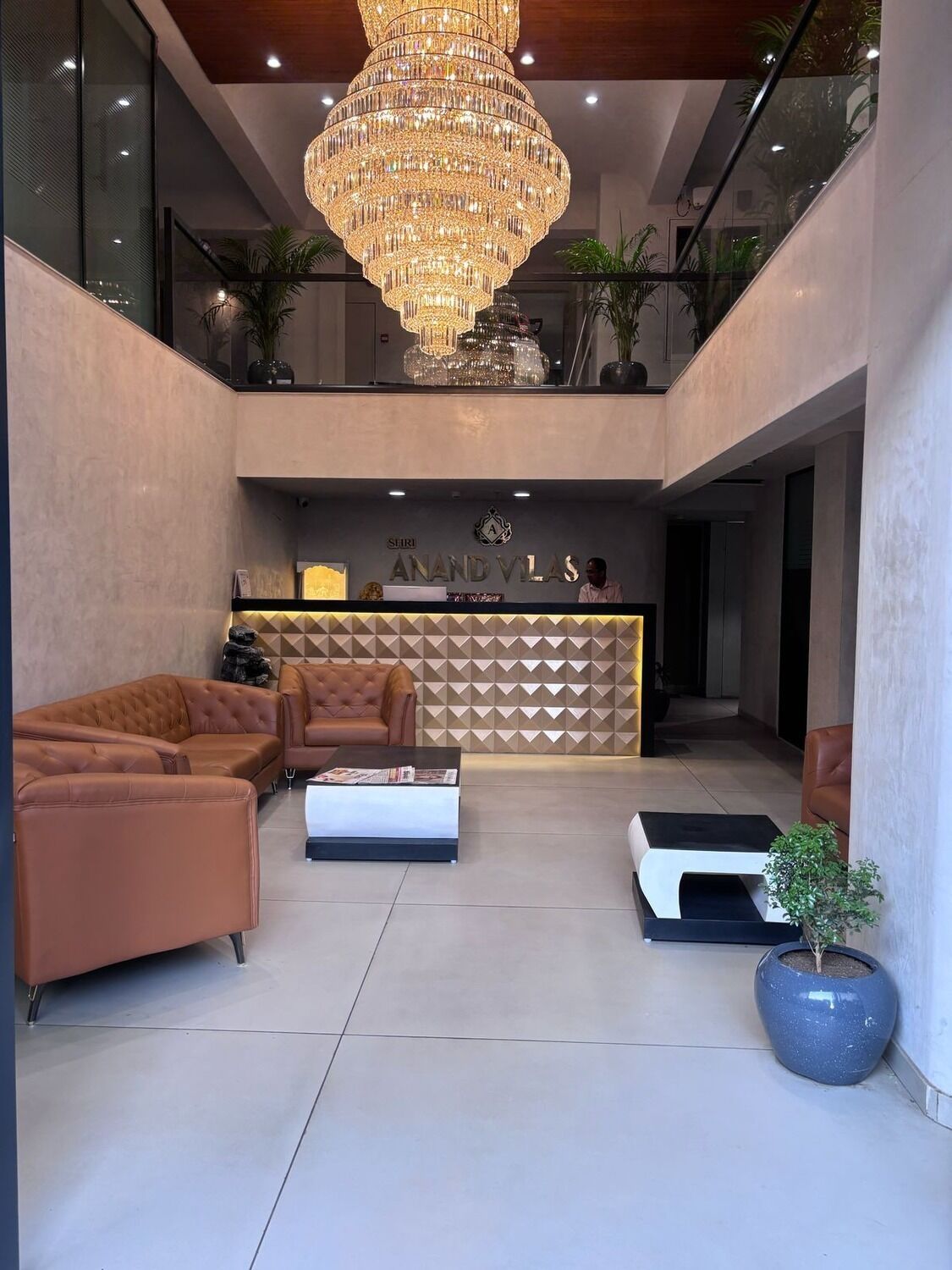 A modern lobby with a chandelier, leather sofas, a reception desk, and a potted plant.