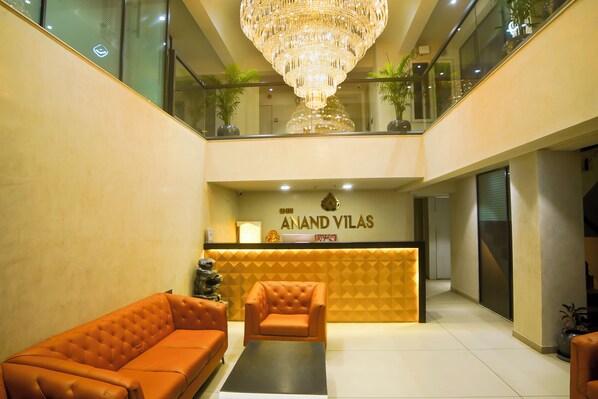 A lobby with a reception desk, a chandelier, and a seating area with two sofas. - Hotel shri anand Vilas (Bhopal)